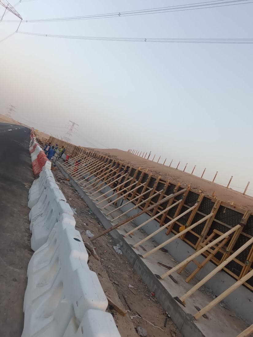 Roadside RC structure — wall formwork, raking props and starter reinforcement, with traffic management maintained to a live carriageway.